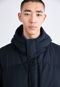 Svart vadderad jacka med hög krage, med en slät yta och minimalistisk design, lämplig för kallt väder.