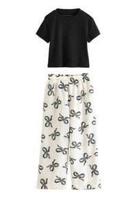 Black, ribbed short-sleeve top paired with cream wide-leg pants featuring a pattern of black bows. Elastic waistband on pants.