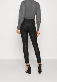 Black faux leather pants with a textured, reptile-like pattern, paired with a gray long-sleeve top and black high-heeled shoes.