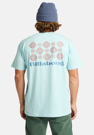 Lyseblå bomulds T-shirt med et farverigt geometrisk mønster på ryggen og ordet "Billabong" i fed, blå skrift.