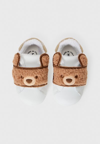 Chaussures blanches à semelle souple avec une sangle en forme de visage d'ours en peluche brun, dotées de détails brodés et de petites oreilles d'ours sur les côtés.