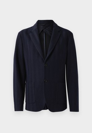 Blazer marine avec motif chevrons, deux poches avant, fermeture à un bouton, et revers crantés, fabriqué à partir d'un tissu texturé.