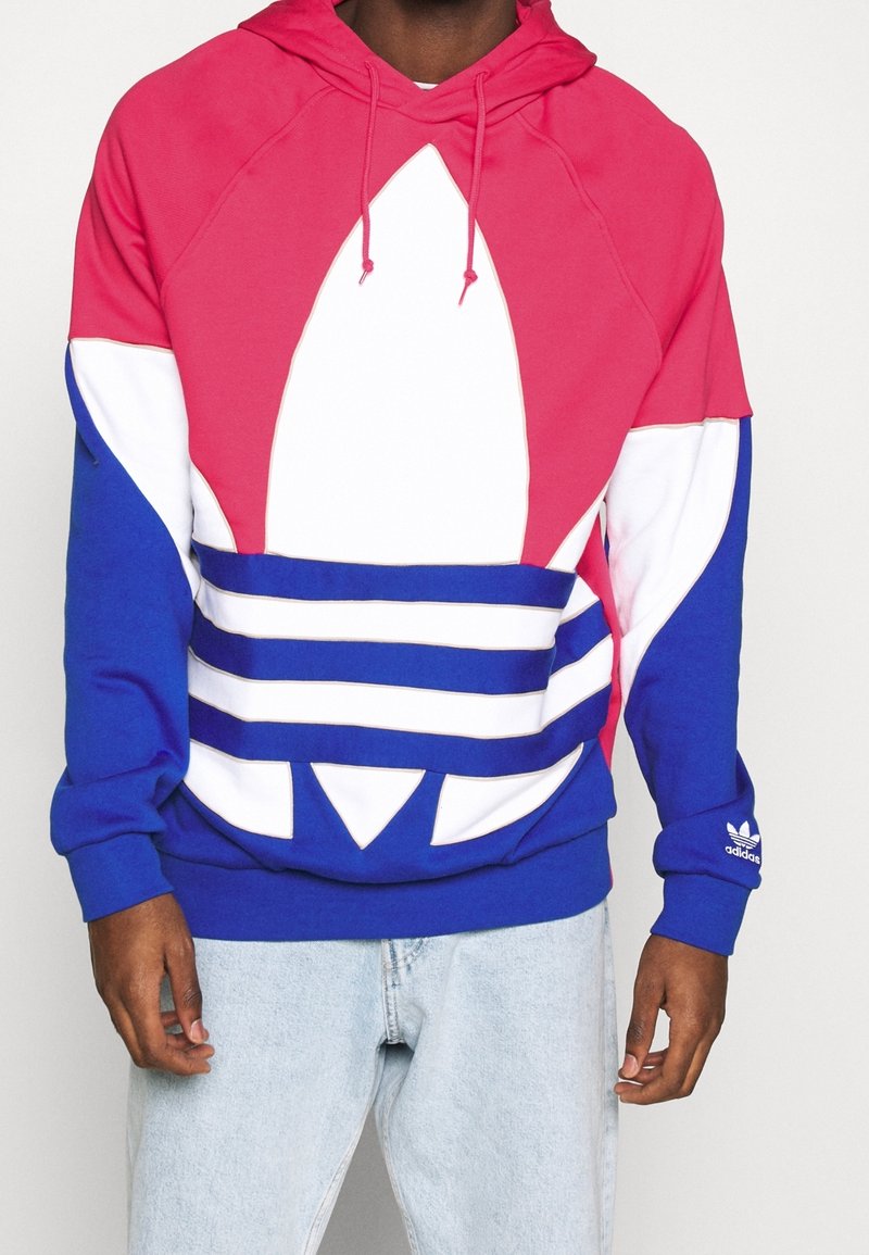 Hoodie med en rosa, vit och blå färgblockdesign, med en stor logotyp och randiga detaljer. Tillverkad av mjukt material.