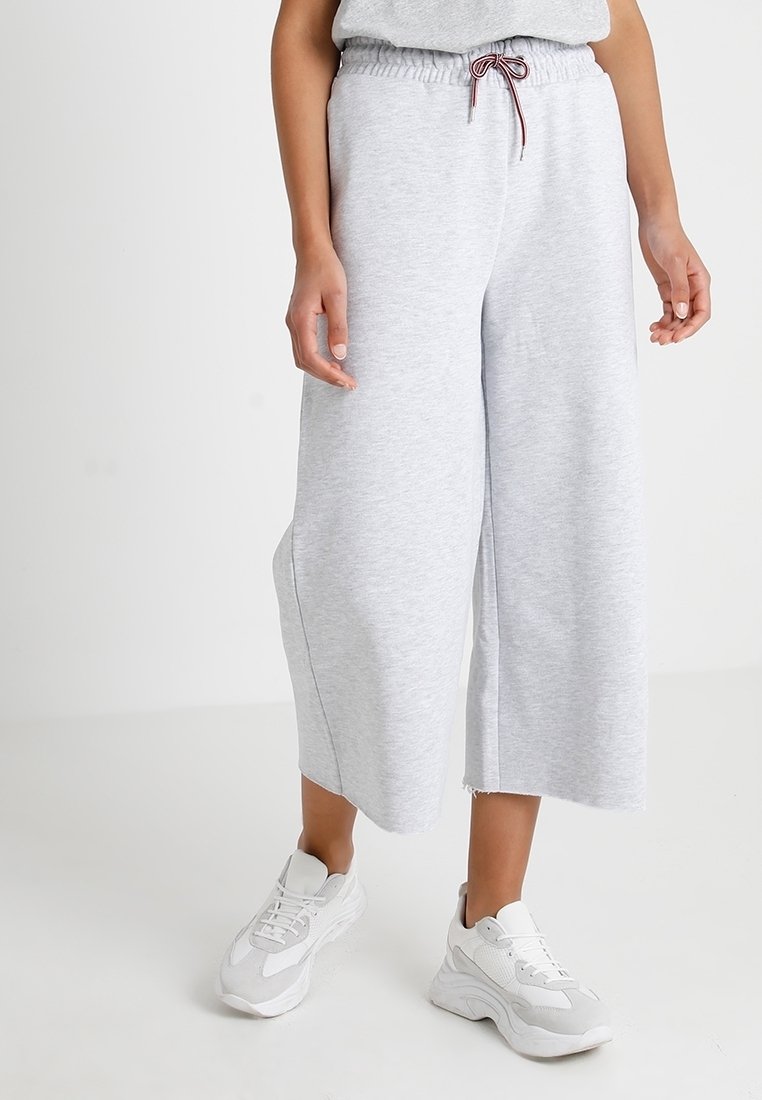 Graue, weit geschnittene Sweatpants mit elastischem Bund und Kordelzug. Baumwollmischgewebe mit rohem Saumdetail. Kombiniert mit weißen Sneakers.