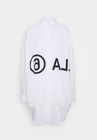 Vit skjorta med knappar och rundad nederkant, prydd med stora svarta textgrafiker på framsidan, inklusive en cirkel och bokstäverna "A.L." i fet stil.