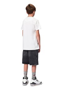 Valkoinen puuvillapaita, mustat farkkushortsit, harmaat sukat ja valkoiset tennarit mustilla yksityiskohdilla. Asu näkyy takaa.