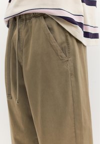 Beige snorebukser med elastisk talje båret sammen med en hvid og navystribet skjorte, der er løst stukket ind.