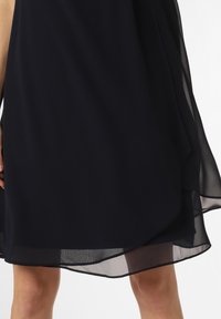 Robe en chiffon navy avec un design doux et fluide, featuring un ourlet superposé légèrement transparent. Texture lisse et tissu léger.
