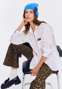 Biała koszula na guziki, spodnie w panterkę, niebieska dzianinowa czapka z metką, czarne masywne loafersy, lekka fakturowana tkanina, luźny krój.