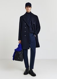Cappotto peacoat in lana blu navy con design a doppiopetto, bottoni grigi, abbinato a un dolcevita a coste blu navy e sciarpa blu, borsa nera e stivali in pelle.