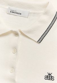 White polo shirt with a black striped collar, three buttons, and an embroidered logo on the chest. Knit texture, minimalist design.