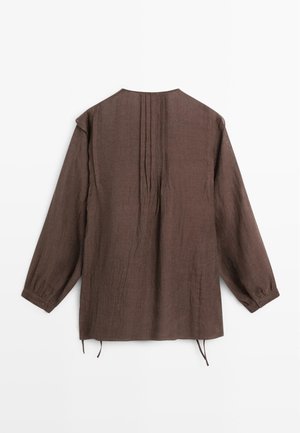 Brązowa bluzka z długim rękawem, plisami na plecach, mankietami na guziki i luźnym krojem, leżąca płasko na białym tle.