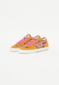 Baskets en daim de couleur jaune vif avec des lacets roses et des accents à motifs multicolores. Semelle en caoutchouc et logo visible sur la languette.