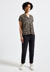 Blusa a maniche corte con stampa leopardata in beige e nero, con scollatura a V, abbinata a jeans neri a gamba affusolata e sneaker bianche.