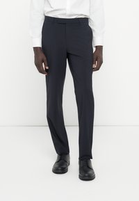 Marineblaue Anzughose aus glattem Stoff, mit taillierter Passform und flachem Vorderteil. Kombiniert mit schwarzen Lederschuhen für einen formellen Look.