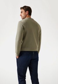 Felpa verde oliva con scollo tondo e polsini a costine, abbinata a jeans in denim scuri. Tessuto liscio e vestibilità comoda.
