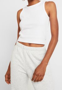 Bílý žebrovaný tílko s vysokým výstřihem, zkráceným střihem a ramínky, doplněné světle šedými tepláky s elastickým pasem.