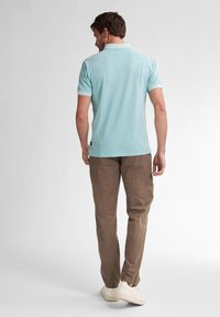 Polo shirt azzurro chiaro con maniche corte e colletto, abbinato a pantaloni beige e sneakers bianche. Tessuto liscio, design minimalista.