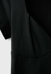 Gros plan d'une robe en tissu noir montrant une manche courte, des détails de couture et une taille froncée.