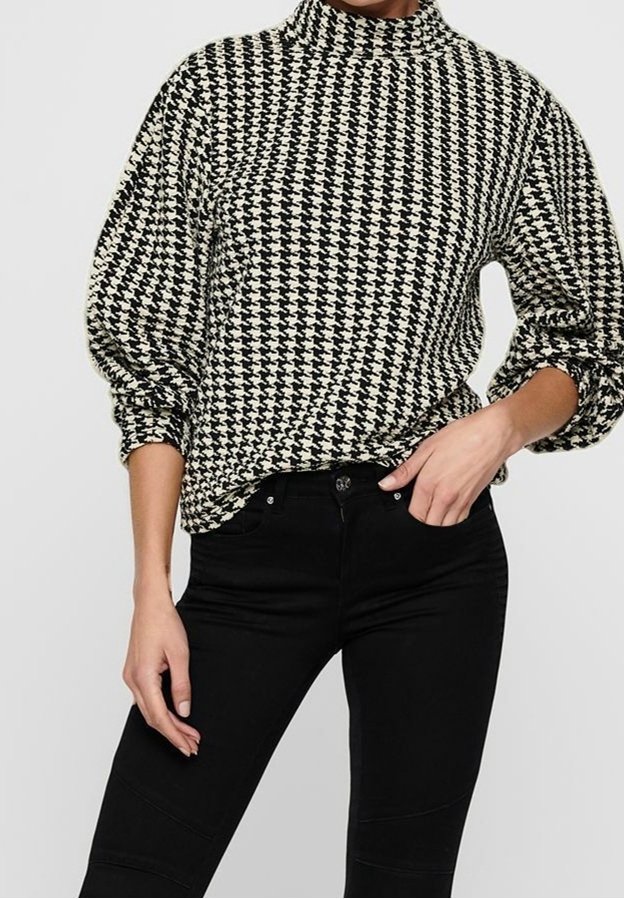 Pull noir et blanc à motif pied-de-poule avec col montant et manches bouffantes, porté avec un jean skinny noir, présentant une texture de tissu lisse.