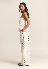 Mustad täpiline rihmadeta topp ja laia säärega püksid heledal taustal, esitades lahtist lõiget ja pükstel taskuid.