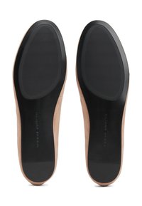 Paire de chaussures plates beiges vues par le dessous, avec semelles en caoutchouc noires texturées et petites sections de talon.