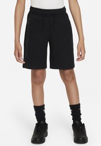 Svarta sportshorts med resårlinning, fickor med dragkedja och ett Nike-logotyp. Matchas med svarta strumpor och sneakers.