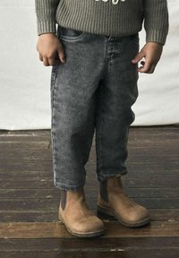Bottines en daim marron avec des panneaux latéraux en élastique, associées à un pantalon en denim gris au fit décontracté avec des ourlets retroussés.
