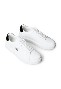 Bílé nízké tenisky s černými patními záložkami, bílými tkaničkami a logem "cK" na straně, zobrazené v páru na bílém pozadí.