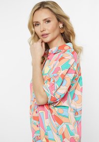 Colorful, printed button-up shirt featuring abstract shapes in coral, blue, and peach. Short sleeves with a soft texture and relaxed fit.