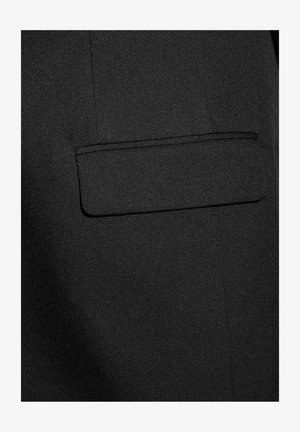 Tissu noir texturé avec une poche rectangulaire sur le côté droit, bordée d'un couturier. Le matériau paraît lisse et brillant.