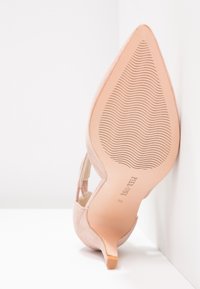 Chaussure à talon haut rose pâle avec un bout pointu et une texture en daim élégante. La semelle est lisse avec un motif ondulé antidérapant. L'étiquette indique "Pier One."