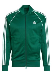 Chaqueta deportiva verde con cremallera, hecha de un tejido suave. Presenta rayas blancas en los hombros y las mangas. Incluye un logotipo bordado.