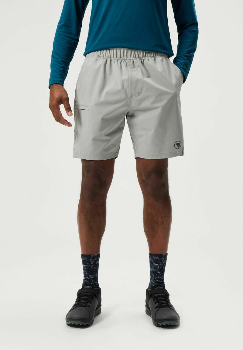 Lichtgrijze shorts met een elastische tailleband, zijzak en logo-detail. Draag met zwarte schoenen en gestreepte marineblauwe sokken.