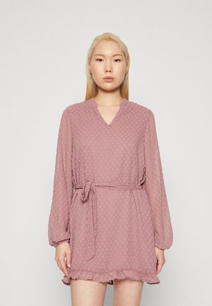 Kort rosa klänning med V-ringning, långa ärmar, texturerade prickar, knytning i midjan och volangkant. Tillverkad av lätt tyg.