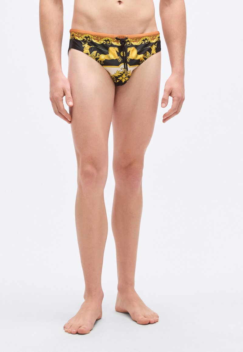 Μαγιό σλιπ με μαύρη βάση και έντονο μοτίβο αλόγων σε κίτρινο και χρυσό. Ελαστική μέση με κορδόνι ρύθμισης· απαλό υφή.