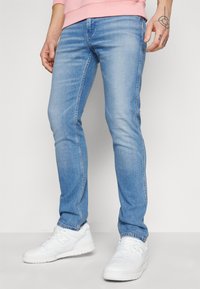 Jasnoniebieskie dżinsy o slim fit, z klasycznym pięciopocketowym krojem i subtelnym wyblaknięciem. Połączone z białymi trampkami.