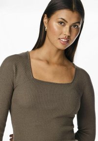 Prążkowany, długi rękaw top w stonowanym brązie z kwadratowym dekoltem. Miękka faktura i dopasowany krój podkreślają sylwetkę. Widoczne złote kolczyki w kształcie kół.