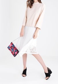 Růžové tričko, bílá plisovaná sukně se spodním krajkovým lemem a barevná květinová kabelka. Černé klínové sandály s otevřenou špičkou dokončují vzhled.