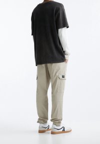 Dark gray oversized t-shirt layered over a white long-sleeve shirt, paired with beige cargo pants and white sneakers with black accents.