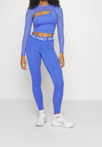 Blå kortärmad topp med utskärningsdetaljer, kombinerad med högmidjade blå leggings med vit midja. Vita träningsskor.