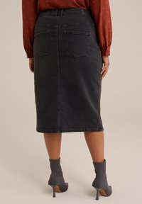 Falda lápiz de mezclilla negra de talle alto con bolsillos traseros, acabada con un dobladillo sin terminar. Combinada con botines grises con tobillo.