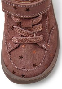 Stivale in suede marrone con motivo a stelle, chiusura con lacci e fascia in velcro. Le cuciture accentuate creano texture lungo il design.
