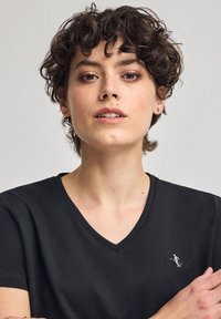 Czarna koszulka z dekoltem w serek, wykonana z miękkiego materiału, z małym haftowanym symbolem osoby w ruchu na klatce piersiowej. Prosty design i dopasowanie.