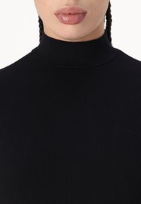 Must mustriba turtleneck-särk kõrge krae ja keha külge jääva disainiga, mis näitab sujuvat tekstuuri ja peent läiget.