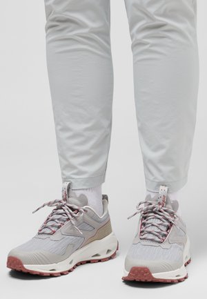 Baskets de sport grises avec un tissu texturé, des accents rouges et une semelle épaisse et à motifs, assorties à un pantalon gris clair et des chaussettes blanches.
