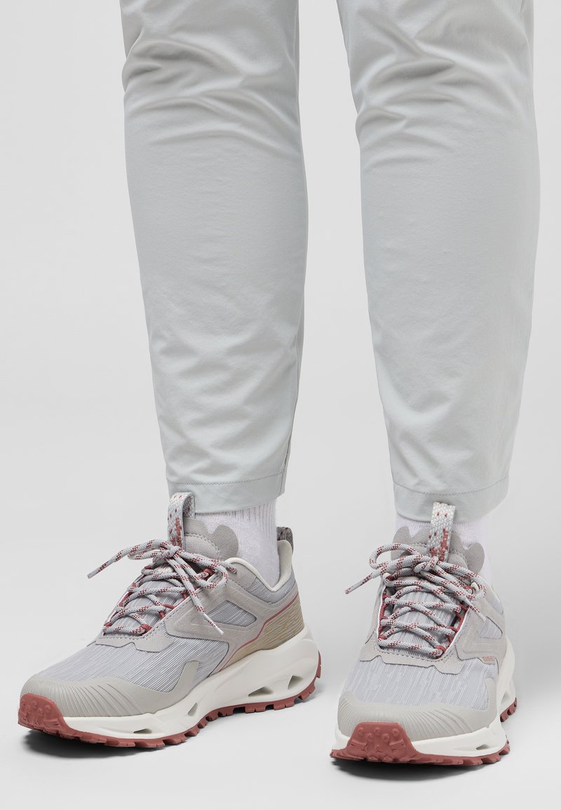 Gray athletic shoes with textured fabric, red accents, and a thick, patterned sole, paired with light gray pants and white socks.