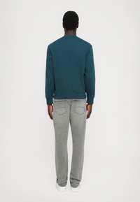 Teal genser med ribbestrikkede mansjetter og kant, kombinert med lysegrå jeans som har baklommer, løs passform, og hvite sneakers.