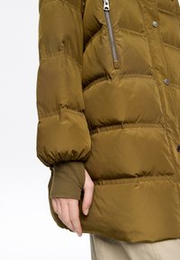 Chaqueta acolchada color verde oliva con diseño acolchado, que incluye un bolsillo lateral con cremallera y un ajuste ceñido en los puños. Textura suave y brillante.