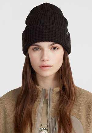 Black ribbed knit beanie with a fold-over cuff, worn over long dark hair, paired with a beige fleece zip-up jacket.
